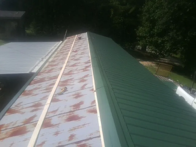 Old rusted panels beside newly installed green metal roofing — Wind Damage Roof Repair by Roofing Brothers in Marrero