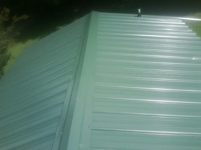 New green metal panels meeting at the ridge of a roof — Flat Roof Repair work by our crew in Marrero