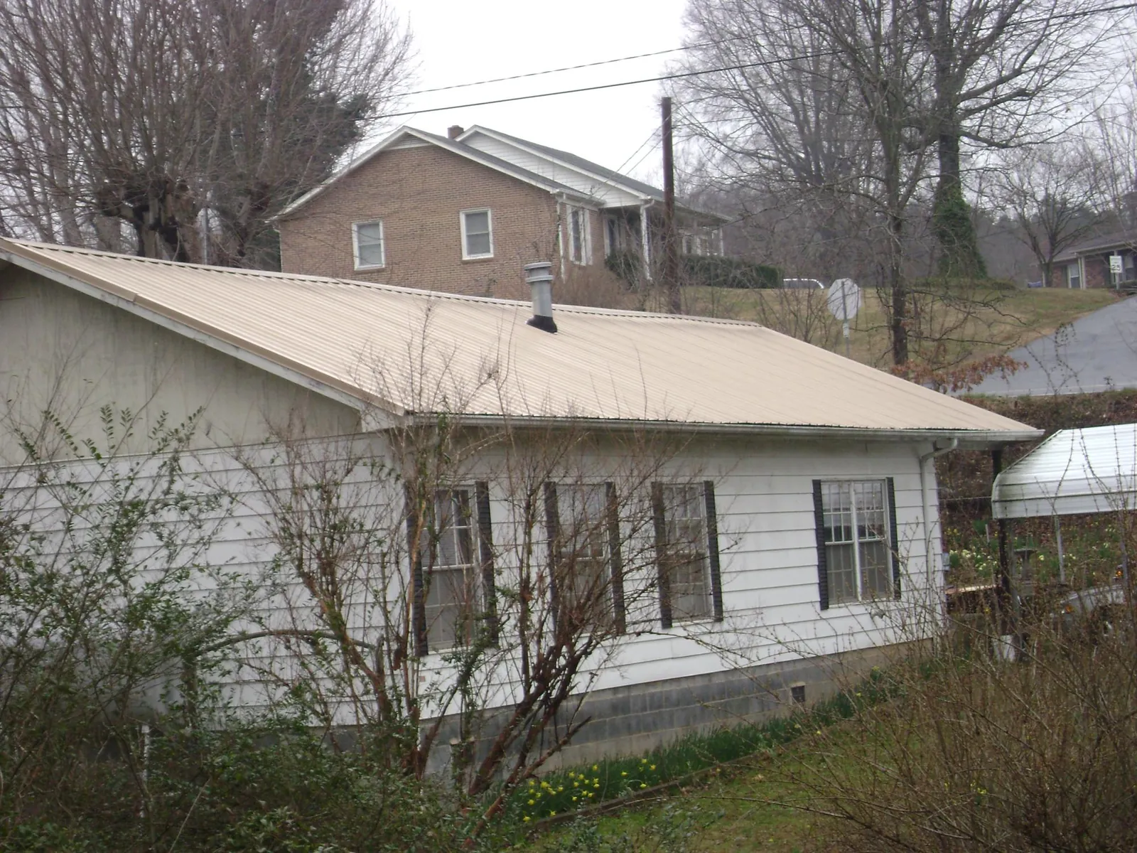 Tan metal roof on a white sided house set into a hillside — Commercial Roofing by Roofing Brothers in Marrero