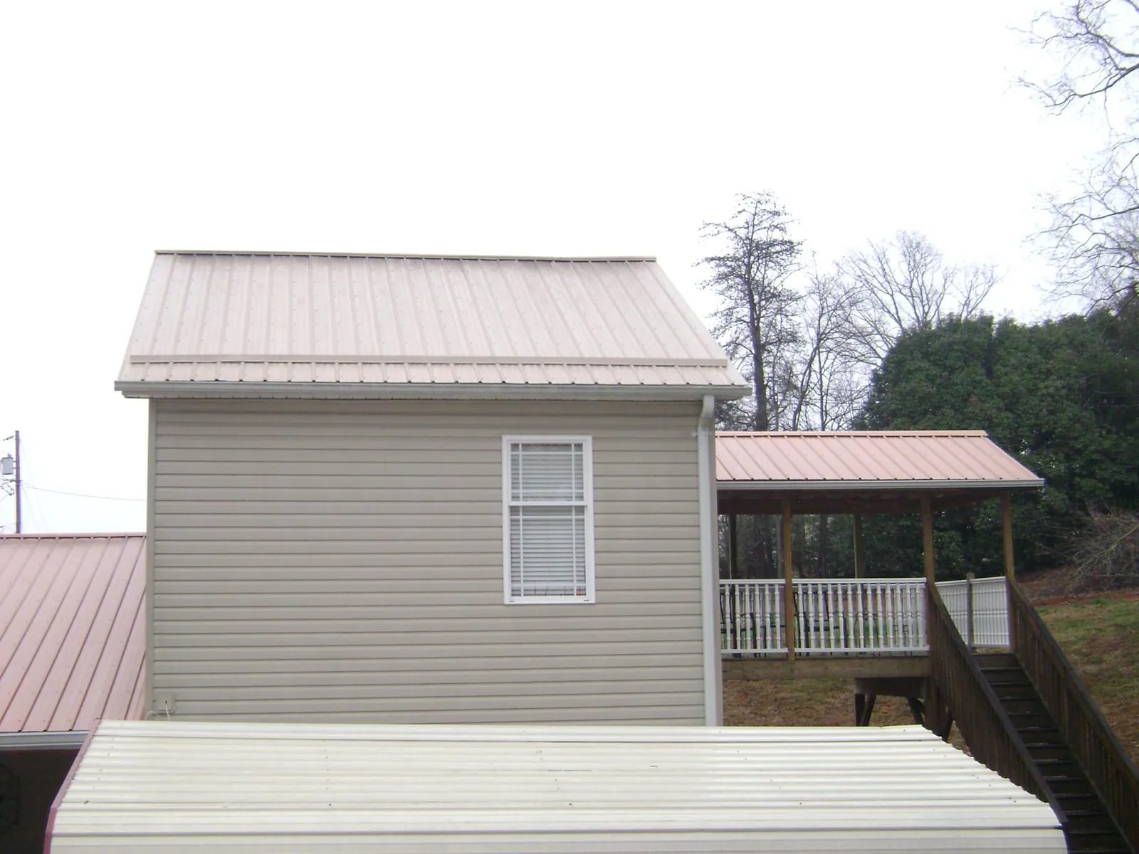Tan metal roofs on a two story addition and attached porch, from a Roof Replacement job in Marrero